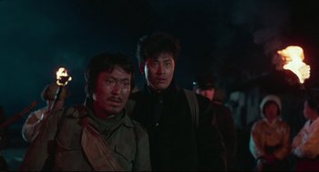 Movie still from “North Korean Partisan in South Korea” (1990), directed by Jeong Ji-yeong – Two men standing next to each other on a dark night; Close Up shot, Low angle
