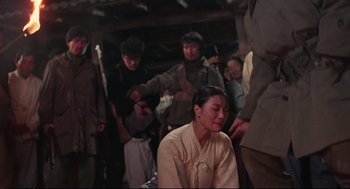 Movie still from “North Korean Partisan in South Korea” (1990), directed by Jeong Ji-yeong – An asian woman sitting in front of a group of people; Medium shot, Over the shoulder angle