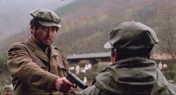 Movie still from “North Korean Partisan in South Korea” (1990), directed by Jeong Ji-yeong – A man holding a gun in front of another man; Medium shot, Over the shoulder angle