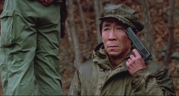 Movie still from “North Korean Partisan in South Korea” (1990), directed by Jeong Ji-yeong – A man holding a gun in his hand while standing next to another man; Close Up shot, Low angle