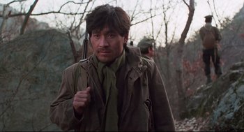 Movie still from “North Korean Partisan in South Korea” (1990), directed by Jeong Ji-yeong – A man holding a rifle while standing in the woods; Medium shot, Low angle