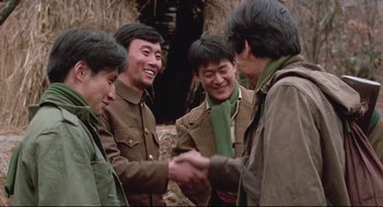 Movie still from “North Korean Partisan in South Korea” (1990), directed by Jeong Ji-yeong – A group of young men shaking hands in front of a stone wall; Medium shot, Over the shoulder angle