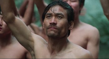 Movie still from “North Korean Partisan in South Korea” (1990), directed by Jeong Ji-yeong – A man with no shirt is looking at the camera; Close Up shot, Low angle