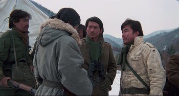 Movie still from “North Korean Partisan in South Korea” (1990), directed by Jeong Ji-yeong – A group of men standing around in the snow with binoculars; Medium shot, Over the shoulder angle