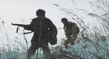 Movie still from “North Korean Partisan in South Korea” (1990), directed by Jeong Ji-yeong – Two men are walking through the tall grass; Medium shot, Low angle