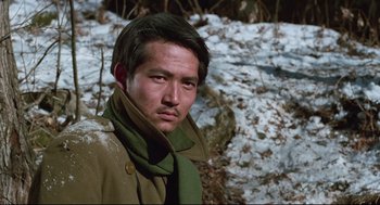 Movie still from “North Korean Partisan in South Korea” (1990), directed by Jeong Ji-yeong – A man wearing a green scarf standing in the snow; Close Up shot, Low angle