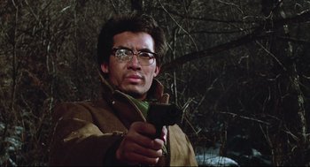 Movie still from “North Korean Partisan in South Korea” (1990), directed by Jeong Ji-yeong – A man holding a gun in a wooded area; Close Up shot, Low angle