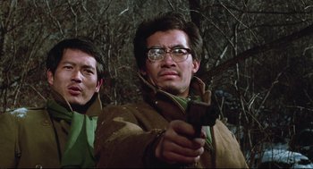 Movie still from “North Korean Partisan in South Korea” (1990), directed by Jeong Ji-yeong – A man holding a gun while standing next to another man; Close Up shot, Low angle