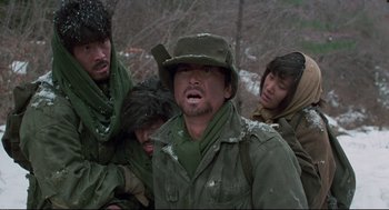 Movie still from “North Korean Partisan in South Korea” (1990), directed by Jeong Ji-yeong – A group of people in the snow with a man in a hat; Medium shot, Over the shoulder angle