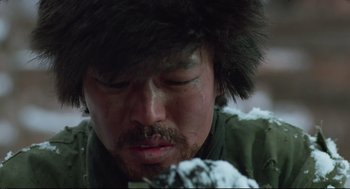 Movie still from “North Korean Partisan in South Korea” (1990), directed by Jeong Ji-yeong – A man with a beard and a hat is looking down at snow; Close Up shot, Low angle