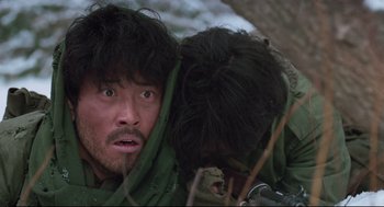 Movie still from “North Korean Partisan in South Korea” (1990), directed by Jeong Ji-yeong – A man with a beard is hiding his face behind another man's head; Close Up shot, Low angle