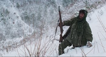 Movie still from “North Korean Partisan in South Korea” (1990), directed by Jeong Ji-yeong – A man holding a rifle while standing in the snow; Medium shot, Low angle