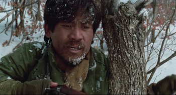 Movie still from “North Korean Partisan in South Korea” (1990), directed by Jeong Ji-yeong – A man with a knife in his mouth near a tree; Close Up shot, Low angle