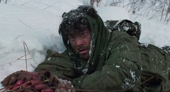 Movie still from “North Korean Partisan in South Korea” (1990), directed by Jeong Ji-yeong – A man in a green jacket is covered in snow; Medium shot, Low angle
