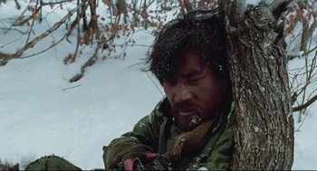 Movie still from “North Korean Partisan in South Korea” (1990), directed by Jeong Ji-yeong – A man in a green jacket sitting next to a tree in the snow; Close Up shot, Low angle