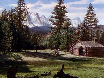 Movie still from “North West Mounted Police” (1940), directed by Cecil B. DeMille – An oil painting of a log cabin in the mountains; Extreme Wide shot, High angle