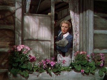 Movie still from “North West Mounted Police” (1940), directed by Cecil B. DeMille – A woman standing at a window looking out of a window; Medium shot, Low angle
