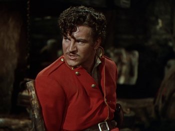Movie still from “North West Mounted Police” (1940), directed by Cecil B. DeMille – A man in a red jacket sitting in a chair; Medium shot, Over the shoulder angle