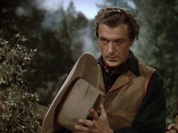Movie still from “North West Mounted Police” (1940), directed by Cecil B. DeMille – A man holding a cowboy hat while standing next to a tree; Close Up shot, Low angle