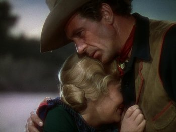Movie still from “North West Mounted Police” (1940), directed by Cecil B. DeMille – A man and a woman embracing each other in a cowboy hat; Medium shot, Low angle