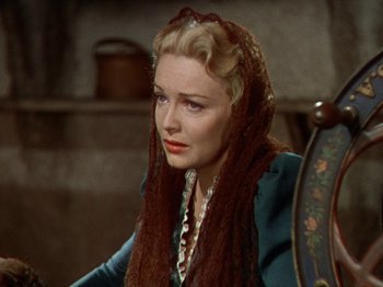 Movie still from “North West Mounted Police” (1940), directed by Cecil B. DeMille – A woman with a scarf on her head sitting in a chair; Close Up shot, Over the shoulder angle