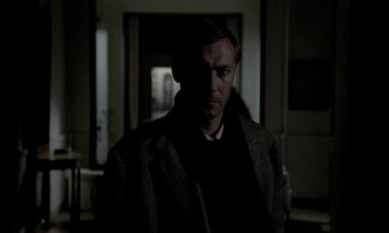 Movie still from “Nostalghia” (1983), directed by Andrei Tarkovsky – A man standing in a dark room with a light shining on him; Close Up shot, Over the shoulder angle