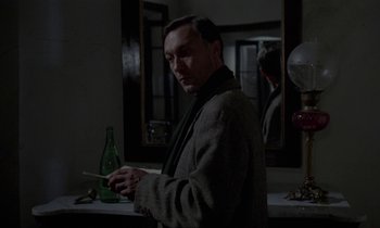 Movie still from “Nostalghia” (1983), directed by Andrei Tarkovsky – A man standing in front of a mirror holding a glass bottle; Medium shot, Over the shoulder angle