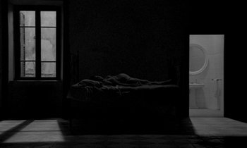 Movie still from “Nostalghia” (1983), directed by Andrei Tarkovsky – A bed in a dark room next to a bath tub; Wide shot, High angle