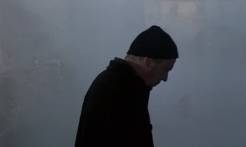 Movie still from “Nostalghia” (1983), directed by Andrei Tarkovsky – An older man in a black coat and a black hat; Medium shot, Over the shoulder angle