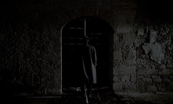 Movie still from “Nostalghia” (1983), directed by Andrei Tarkovsky – A man standing in front of a door in a dark room; Wide shot, Low angle