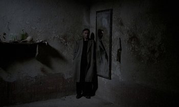 Movie still from “Nostalghia” (1983), directed by Andrei Tarkovsky – A man standing in front of a mirror in a dark room; Wide shot, High angle