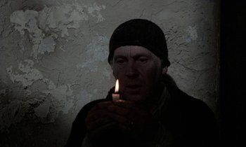 Movie still from “Nostalghia” (1983), directed by Andrei Tarkovsky – A man holding a lit candle in a dark room; Close Up shot, High angle