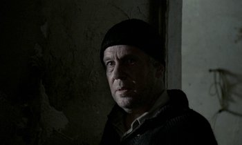 Movie still from “Nostalghia” (1983), directed by Andrei Tarkovsky – A man wearing a black hat standing next to a wall; Close Up shot, Over the shoulder angle