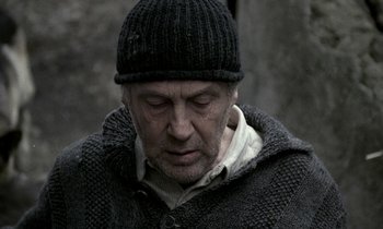 Movie still from “Nostalghia” (1983), directed by Andrei Tarkovsky – An older man wearing a black hat and a sweater; Close Up shot, Over the shoulder angle