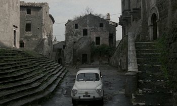 Movie still from “Nostalghia” (1983), directed by Andrei Tarkovsky – An old car parked in an abandoned area; Extreme Wide shot, High angle