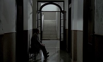 Movie still from “Nostalghia” (1983), directed by Andrei Tarkovsky – A man sitting on a chair in a hallway; Wide shot, High angle