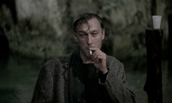 Movie still from “Nostalghia” (1983), directed by Andrei Tarkovsky – A man is smoking a cigarette outside in the rain; Close Up shot, Low angle