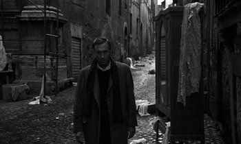 Movie still from “Nostalghia” (1983), directed by Andrei Tarkovsky – A black and white photo of a man standing in the middle of an alley; Medium shot, Low angle