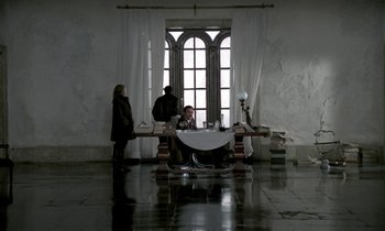 Movie still from “Nostalghia” (1983), directed by Andrei Tarkovsky – A group of people standing around a table in front of a window; Wide shot, High angle