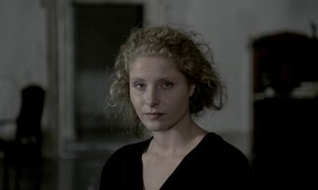 Movie still from “Nostalghia” (1983), directed by Andrei Tarkovsky – A woman with curly blonde hair wearing a black shirt; Close Up shot, Over the shoulder angle