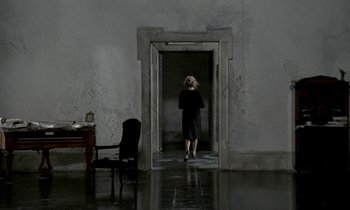 Movie still from “Nostalghia” (1983), directed by Andrei Tarkovsky – A woman standing in front of an open door in a dark room; Wide shot, High angle