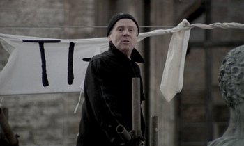 Movie still from “Nostalghia” (1983), directed by Andrei Tarkovsky – An old man in a black coat and a black hat is standing by a clothesline; Medium shot, Low angle