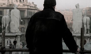 Movie still from “Nostalghia” (1983), directed by Andrei Tarkovsky – A man in a black jacket looking out over a city; Medium shot, Over the shoulder angle