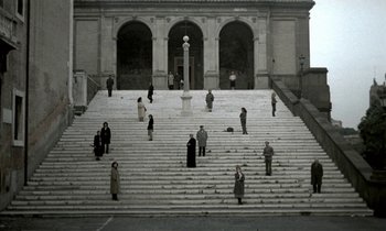 Movie still from “Nostalghia” (1983), directed by Andrei Tarkovsky – A group of people standing on top of a set of stairs; Extreme Wide shot, High angle