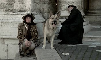 Movie still from “Nostalghia” (1983), directed by Andrei Tarkovsky – A man and a woman sitting on a step next to a dog; Wide shot, Low angle