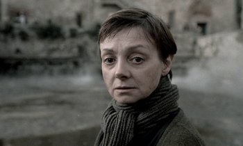 Movie still from “Nostalghia” (1983), directed by Andrei Tarkovsky – A woman wearing a sweater and a scarf looking at the camera; Close Up shot, Over the shoulder angle