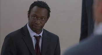 Movie still from “Notes on a Scandal” (2006), directed by Richard Eyre – A man in a suit and tie standing in front of a white wall; Close Up shot, Over the shoulder angle