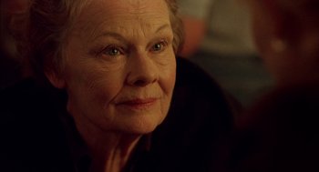 Movie still from “Notes on a Scandal” (2006), directed by Richard Eyre – An older woman looking at the camera while sitting down; Close Up shot, Over the shoulder angle