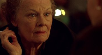 Movie still from “Notes on a Scandal” (2006), directed by Richard Eyre – An older woman looking at the camera in a dark room; Close Up shot, Over the shoulder angle