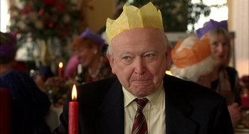 Movie still from “Notes on a Scandal” (2006), directed by Richard Eyre – An older man wearing a paper crown with candles in the background; Close Up shot, Over the shoulder angle